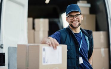 Portrait of happy worker unloading boxes from a delivery van and looking at camera.